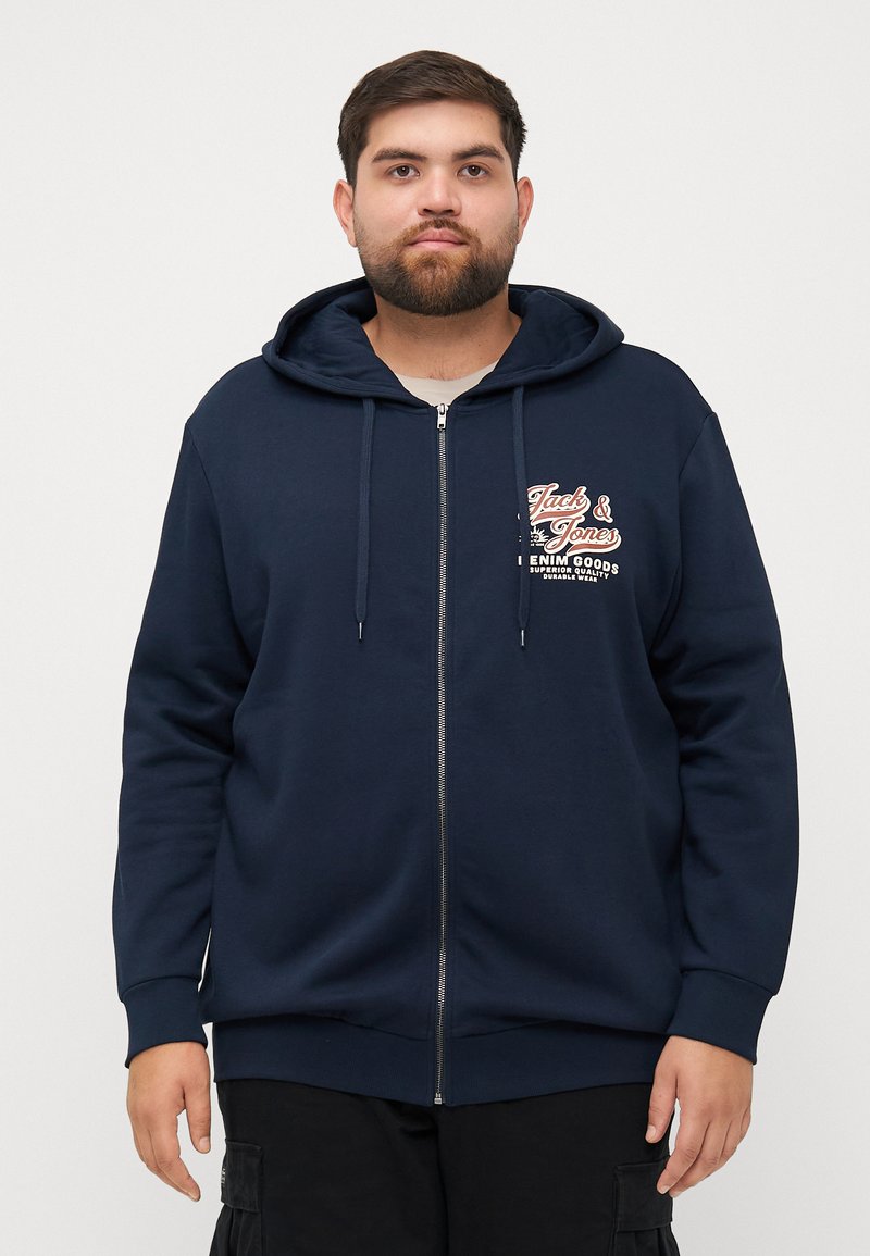 Navy zip-up hoodie in soft fabric, featuring a front graphic logo, drawstring hood, and ribbed cuffs and hem. Classic, relaxed fit.