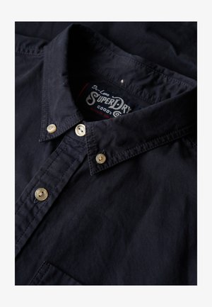 Mørkeblå skjorte med knapper lavet af bomuld med en blød tekstur, der har en klassisk krave og elfenbensfarvede knapper, mærket label indeni kraven.