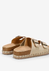 Sandalias beige con dos hebillas ajustables, plantilla de corcho y entresuela de yute trenzado. Diseño perforado para ventilación y estilo casual.
