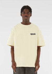 Light yellow oversized t-shirt made of cotton, featuring short sleeves and a black text design on the left chest area.