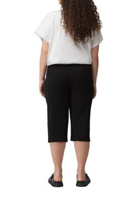 Zwarte capri broek met een gladde textuur, voorzien van een rechte snit, achterzakken, gecombineerd met een losse witte T-shirt met korte mouwen.
