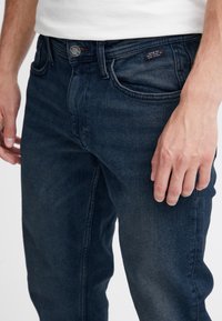 Mørkeblå denimjeans med klassisk fem-lommers design, knappelukking og subtil falming på frontpanelet.