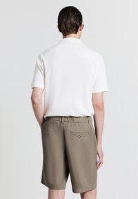 Weißes, strukturiertes Poloshirt mit kurzen Ärmeln, kombiniert mit khakifarbenen Shorts mit Gesäßtaschen und einem elastischen Bund.