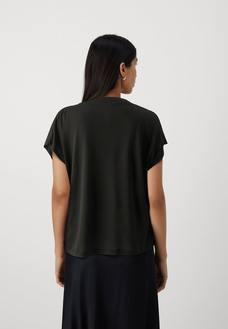 Schwarzes kurzes T-Shirt aus leichtem Stoff, mit lockerer Passform und abgerundetem Saum; getragen mit einem langen schwarzen Rock.