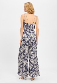 Jumpsuit floreale di colore blu navy con fiori color crema; sul retro presenta spalline sottili e una vestibilità comoda, design a gamba larga. Texture liscia, drappeggio elegante.