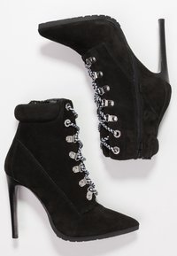 Black suede ankle boots with pointed toes, decorative silver hardware, black and white laces, and a high stiletto heel. Side zipper detail.