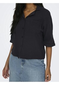 Dark navy short-sleeve shirt made of textured fabric with a button front and single chest pocket, paired with a light blue denim skirt.