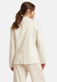 Helle beige Blazer mit vertikalen Streifen; verfügt über einen taillierten Schnitt, einen Reverskragen und einen Einzelsschlitz hinten für zusätzliche Struktur.