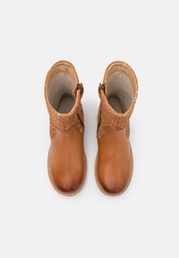 Bottes chelsea en cuir marron avec un dessus texturé, fermeture éclair sur le côté et une semelle lisse contrastante. Détails en tan et en coutures présents.