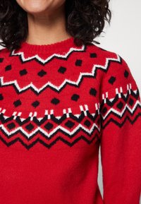 Czerwony sweter z dzianiny z geometrycznym wzorem czarno-białych zygzaków, diamentów i kropek na yoke. Miękka tekstura i okrągły dekolt.