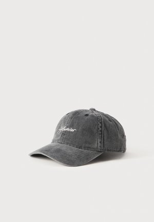 Une casquette de baseball délavée gris anthracite, avec une visière courbée et une broderie blanche en écriture cursive, sur un fond clair uni.