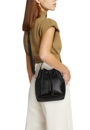 Svart läderväska med dragsko och ljus sömnad. Har en avtagbar rem och en texturerad yta.