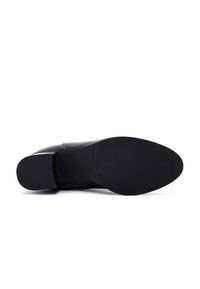 Bottine en cuir noir avec un bout arrondi, une texture lisse et un petit talon carré. La semelle est en caoutchouc avec une finition plate.