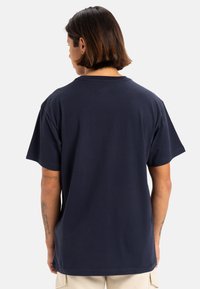 Camiseta de algodón azul marino con un corte holgado, cuello redondo y mangas cortas; cuenta con detalles de costura y una textura suave.