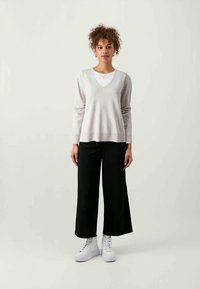 Világosszürke V nyakú pulóver hosszú ujjakkal, fekete, bőszárú nadrággal és fehér, magasszárú sportcipővel párosítva. Egyszerű, laza dizájn.