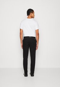 Pantaloni neri a vestibilità slim, realizzati in un tessuto liscio. Presentano passanti per cintura, tasche posteriori e un logo discreto sulla vita.