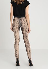 Pantalones skinny de estampado de serpiente beige con un patrón texturizado, combinados con una blusa negra de manga corta y zapatos de tacón alto negros.