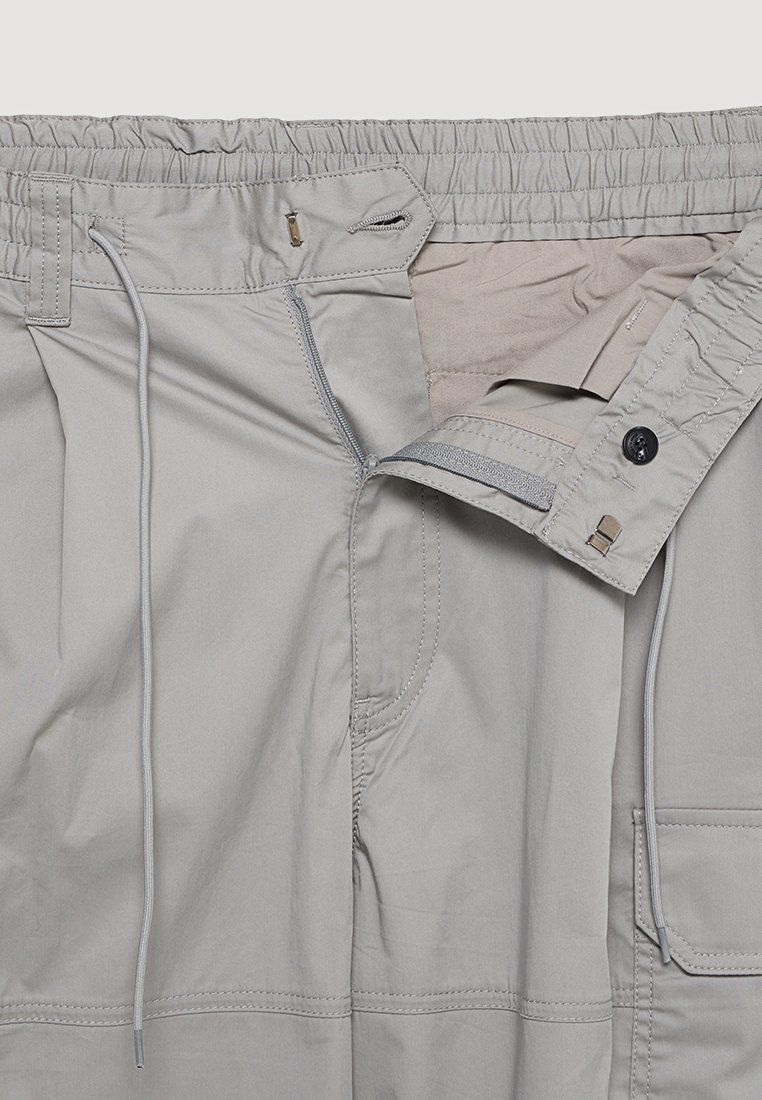Pantalones gris claro con cintura elástica, cordón ajustable, cierre con cremallera y botón, y bolsillos laterales, con una textura suave.