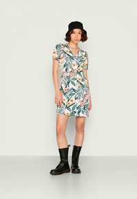 Vestido curto floral com padrões tropicais em verde e rosa, mangas bufantes e decote quadrado; combinado com botas de combate pretas com atacadores.