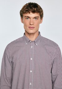 Camisa de manga larga con botones, en un patrón a cuadros en color burdeos y blanco. Dispone de cuello y se abrocha mediante botones en la parte delantera. Tejido de algodón.