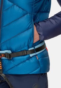 Gilet isolante blu con motivo a rombi, maniche blu navy in contrasto e cintura in vita nera regolabile con dettagli arancioni e blu.