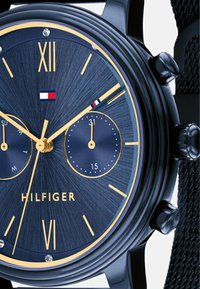 Vyrų laikrodis su mėlynu tekstūruotu ciferblatu, auksinėmis valandų žymomis, dviem subdials ir juodu tinkleliu. Rodyklių logotipas "HILFIGER".