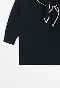 Black short-sleeve sweater with white trim on cuffs and a tied scarf neckline with white edging on a plain background.