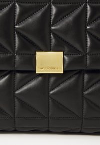 Czarna pikowana skórzana torba z geometrycznym wzorem, ozdobiona złotym kwadratowym zapięciem z wygrawerowanym napisem "KARL LAGERFELD."
