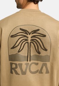 Sweatshirt beige avec un design texturé de palmier en marron foncé et les lettres "RVCA" en bas, sur un fond semblable à un filet.