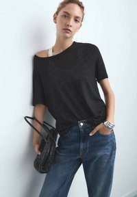 Camiseta negra de gran tamaño con un corte holgado, mangas cortas y un drapeado relajado. Combinada con unos jeans de mezclilla azul de cintura alta y un bolso negro de fibra tejida.
