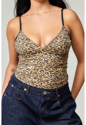 Kobieta ubrana w bezrękawnik w panterkę z cienkimi czarnymi ramiączkami i wysokimi ciemnoniebieskimi dżinsami, z rękami w kieszeniach.