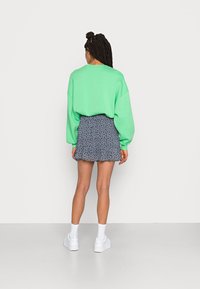 Mintgrüner, übergroßer Pullover mit abgesenkten Schultern, kombiniert mit einem marineblauen, gemusterten Minirock. Weiße Sneaker und Knöchelsocken runden den Look ab.