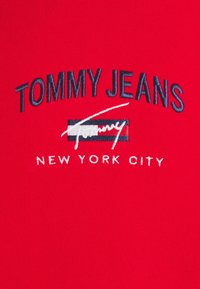 T-shirt in cotone rosso con testo ricamato: "TOMMY JEANS" in blu navy, "NEW YORK CITY" in bianco, con un logo stilizzato al centro.