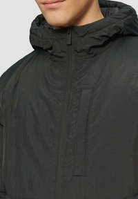 Zwarte lichtgewicht jas met een ritssluiting aan de voorkant, verstelbare capuchon en een soepele textuur. Inclusief een voorzak met een subtiele naaddetail.