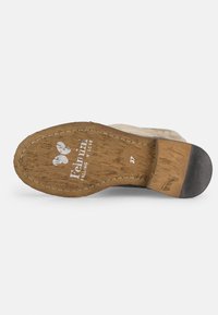 Suela de zapato de madera marrón con un tacón de goma y un logotipo grabado. Presenta un patrón texturizado y una marcación de tamaño, posicionada sobre un fondo blanco.