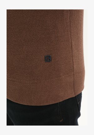 Pruun tekstuurne kampsun, millel on soonikdisain, väike must logo äär ja selge siluett, koos tumehallide teksadega.