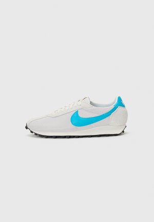 Sneakers Nike z białą siateczkową cholewką, turkusowym logo w formie "swoosh" i zamszowym akcentem na pięcie. Czarna gumowa podeszwa o płaskim profilu.