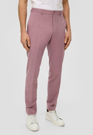 Pantalon rose clair avec une coupe ajustée, doté d'une fermeture à bouton, d'une texture lisse et de poches latérales, associé à des baskets blanches.
