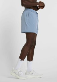 Light blue shorts with an elastic waistband and side pockets, paired with white sneakers and socks. The shorts are smooth-textured.