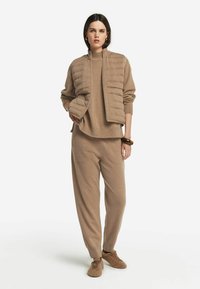 Beige puffer-jacka med ribbad krage, lagrad över en matchande beige stickad tröja och sweatpants. Mjuk textur och avslappnad passform.