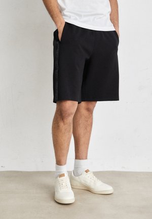 Mustat shortsit, jotka on valmistettu puuvillasekoitteesta. Niissä on joustava vyötärönauha ja sivutaskut sekä hienovarainen Calvin Kleinin logo sivulla.