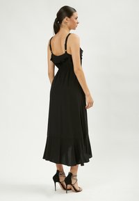 Abito maxi nero con spalline volantee, vita elasticizzata e orlo svasato. Abbinato a tacchi alti neri con cinturini. Tessuto liscio e leggero.