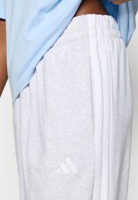 Világosszürke melegítőnadrág fehér csíkokkal az oldalán. Puha tapintású, rugalmas derékpánttal és finom, fehér logóval.