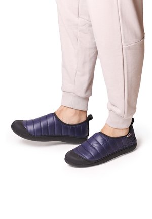 Tumedat quiltitud libisemised kingad musta kummist tallaga ja ümmarguse varbaga. Ülemine osa on kaetud pehme ja tekstuuriga pinnaga mugavuse tagamiseks.