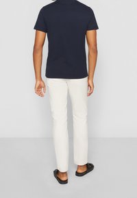 Camiseta corta de algodón en color marino, combinada con pantalones color crema y sandalias negras de tipo deslizante, exhibiendo un ajuste casual y relajado.