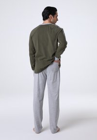 Pantaloni sportivi grigi e una maglietta a maniche lunghe verde oliva. La maglietta presenta accenti grigi a contrasto lungo le maniche e il collo.
