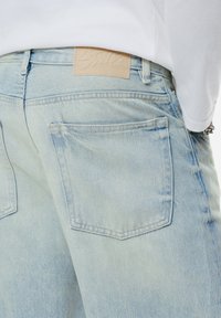 Jeans din denim de culoare albastru deschis, cu un finisaj texturat. Au un petic din piele bej pe talie și două buzunare la spate.