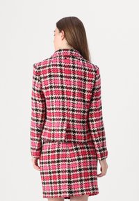 Rosa und schwarze kariert gemusterte Anzug mit einem taillierten Blazer und einem körperbetonten Rock, aus strukturiertem Stoff mit einem gestalteten Kragen.