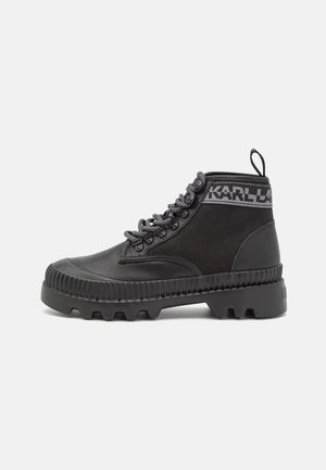 Sort højtopstøvle med tyk kraftig sål, tekstureret tåhætte, stofsider, forstærkede snørebånd og "KARL LAGERFELD" branding rundt om anklen.