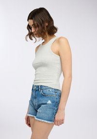 Jasnoszara, prążkowana bluzka na ramiączkach w połączeniu z podartymi niebieskimi szortami dżinsowymi z postrzępionymi brzegami. Gładka faktura i dopasowany krój.